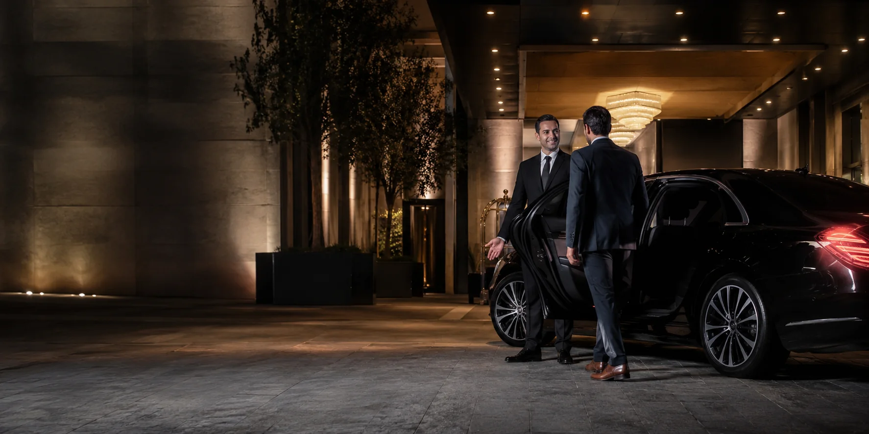 Professional chauffeur welcoming a guest beside a black luxury sedan at an elegant Los Angeles hotel